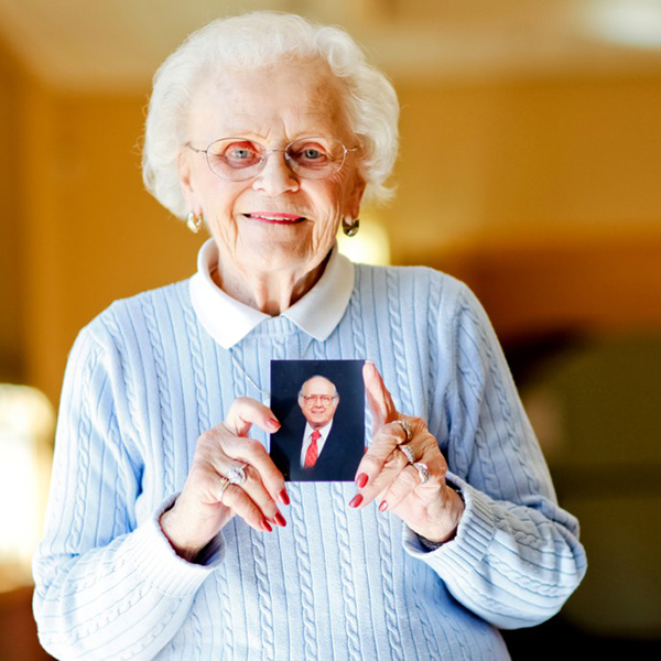 Elderly woman smiling, holding picture of a man