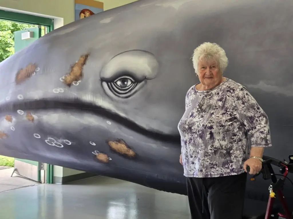 Senior citizen standing in front of a giant inflatable whale.