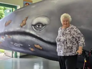 Senior citizen standing in front of a giant inflatable whale.