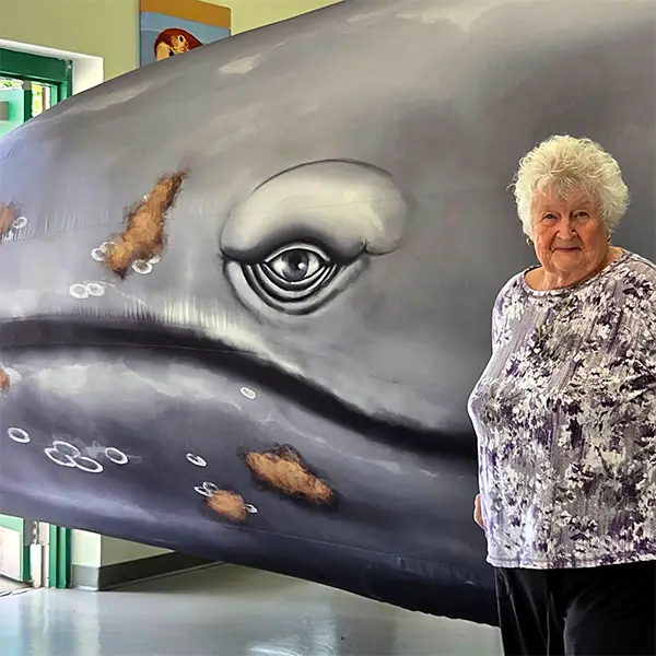 Senior citizen standing in front of a giant inflatable whale.